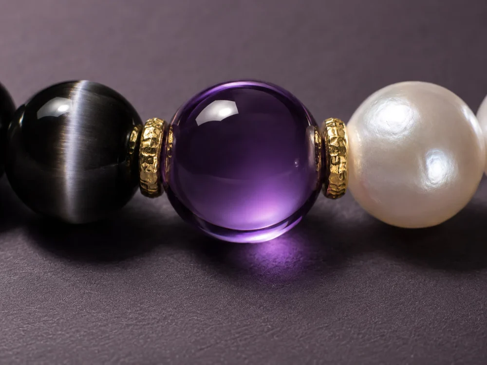 Extreme close-up of chatoyant cat's eye obsidian, radiant natural pearl, and polished 18k gold-filled spacer beads.