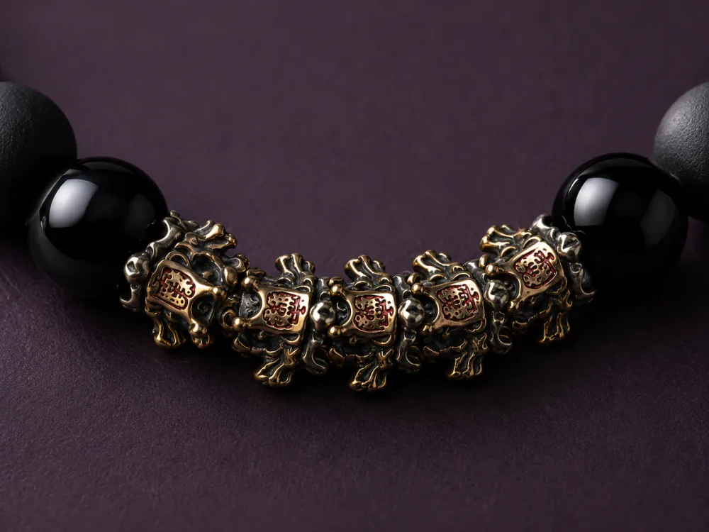 Extreme macro close-up of 9Purple bracelet showing intricate engravings on vintage gold and silver patina metal beast charms with tiny red dots and sharp catchlights on glossy black beads.