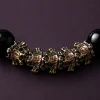 Extreme macro close-up of 9Purple bracelet showing intricate engravings on vintage gold and silver patina metal beast charms with tiny red dots and sharp catchlights on glossy black beads.
