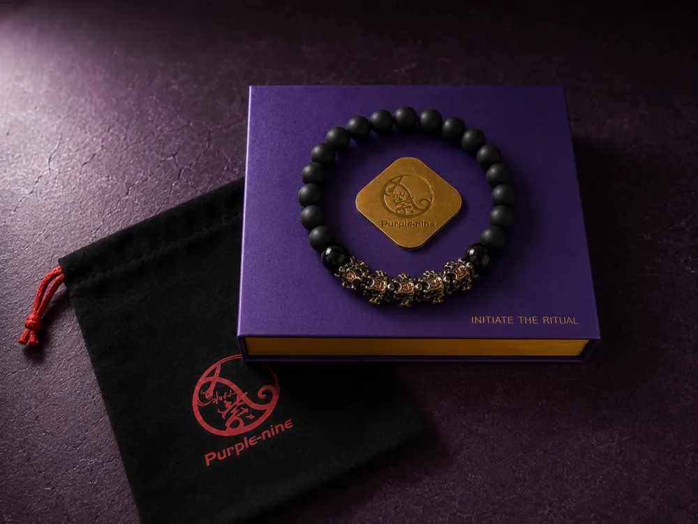 9Purple closed purple luxury gift box with a gold logo medallion and gold text 'INITIATE THE RITUAL', featuring the obsidian bracelet flat on top and a black velvet drawstring bag.