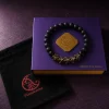 9Purple closed purple luxury gift box with a gold logo medallion and gold text 'INITIATE THE RITUAL', featuring the obsidian bracelet flat on top and a black velvet drawstring bag.