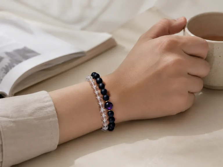 Double-stacked 9Purple natural stone bracelets featuring matte black obsidian and clear quartz beads with a signature royal purple center anchor held intimate with a warm ceramic cup