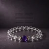 Water Flow bracelet with clear quartz beads, purple amethyst center bead, and gold-plated spacers on dark textured background