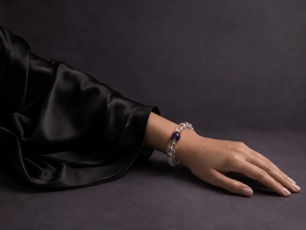 Water Flow bracelet worn on female wrist with clear quartz beads, purple amethyst center bead, and gold-plated spacers