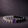 9Purple Yin-Yang Balance single-strand bracelet featuring matte black obsidian, clear white crystal beads, and a central purple amethyst on a dark slate background.