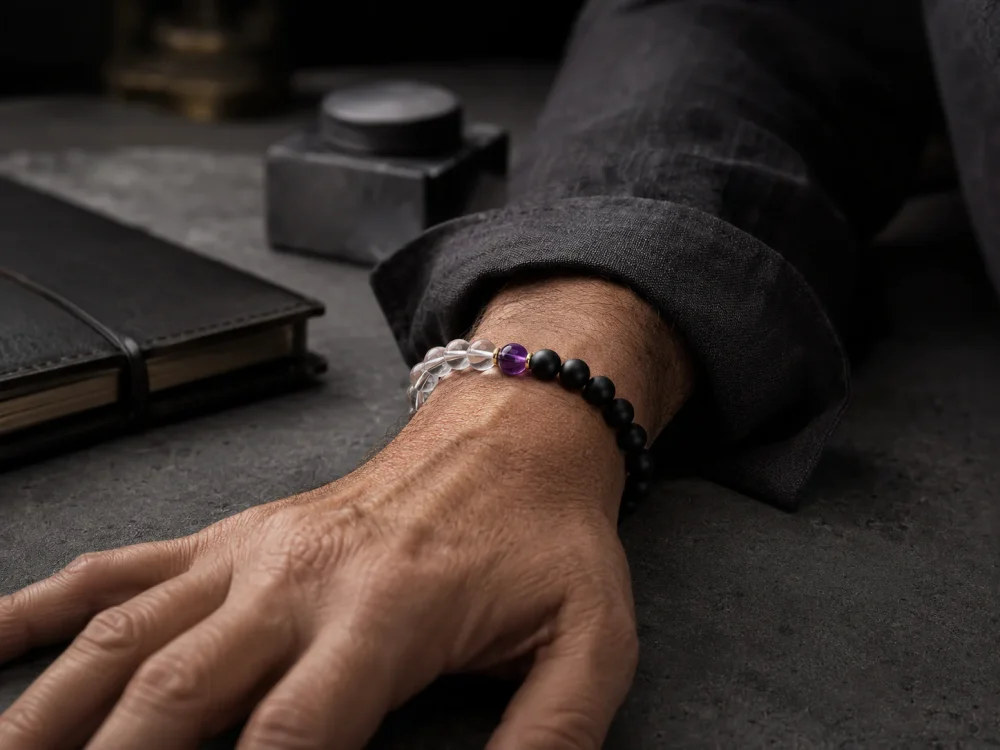 A successful mature man wearing the 9Purple Yin-Yang Balance single-strand bracelet on his wrist, resting on a dark concrete desktop.