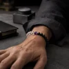 A successful mature man wearing the 9Purple Yin-Yang Balance single-strand bracelet on his wrist, resting on a dark concrete desktop.