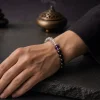 An elegant mature woman wearing the 9Purple Yin-Yang Balance bracelet on her wrist, resting her hand on a modern Zen slate desktop.