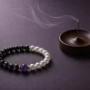 9Purple protective talisman bracelet resting next to a modern bronze incense burner with ethereal smoke.