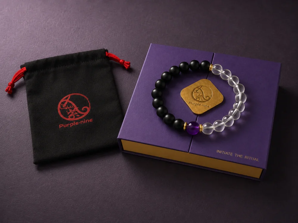 The 9Purple Yin-Yang bracelet draped obliquely across the top edge of the deep purple rectangular luxury packaging box with gold foil logo.