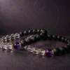 Two identical 9Purple Yin-Yang Balance bracelets intertwined in a non-intersecting elegant curve on a dark grey textured slate background.