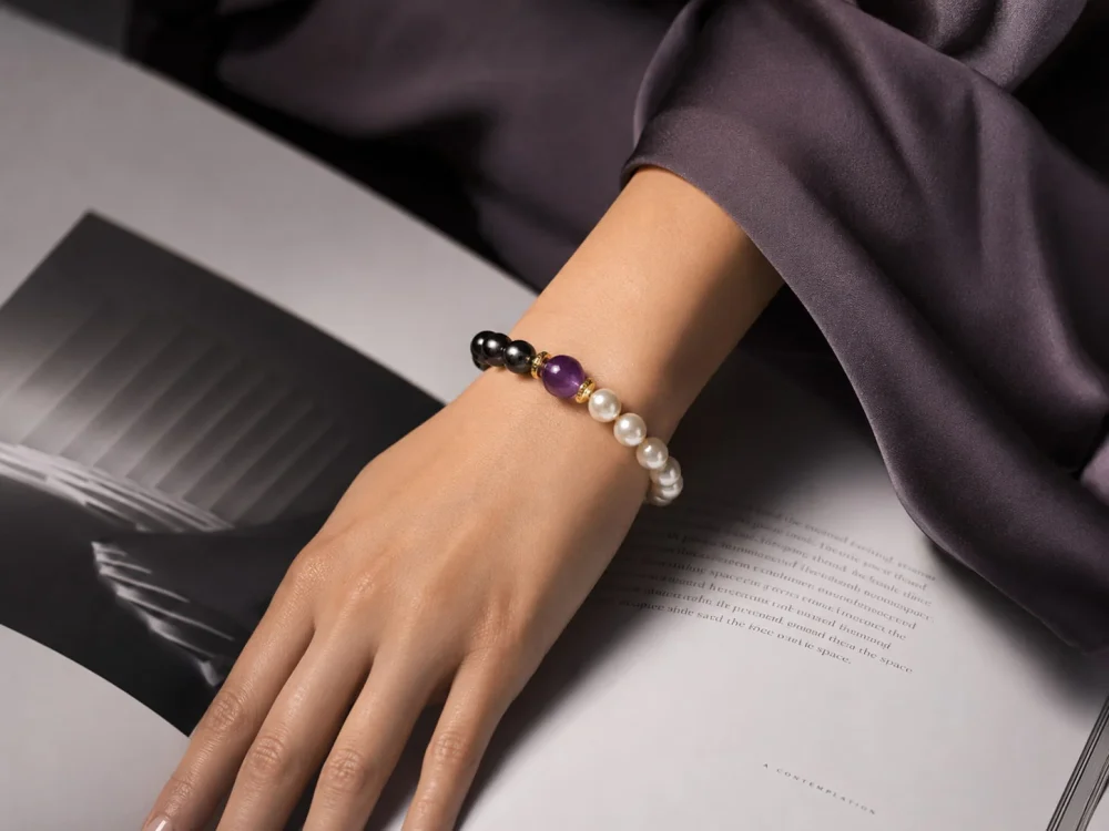 Close-up of a stylish hand wearing the 9Purple pearl and obsidian bracelet resting on a contemporary desk setup.