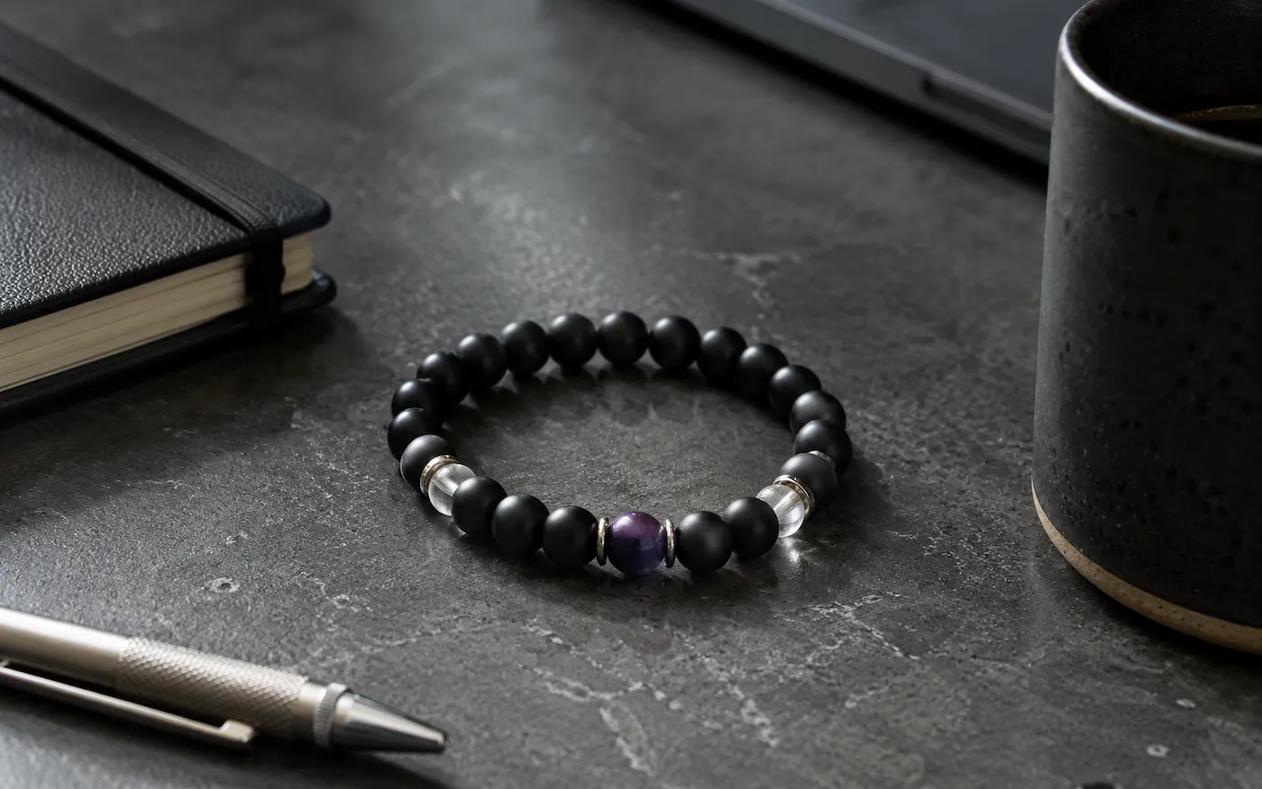 Architectural composition capturing premium men's stone bracelets arranged on a brutalist workspace desk under low-key directional lighting shadows