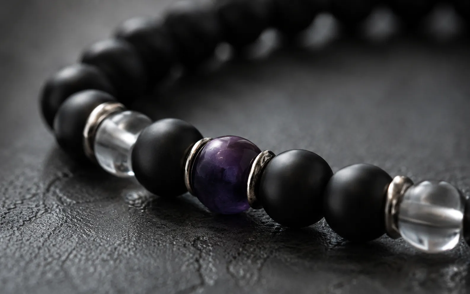 Macro detail close up highlighting a 9Purple men's bracelet with light-absorbing black obsidian and a single royal purple center bead under deep chiaroscuro lighting