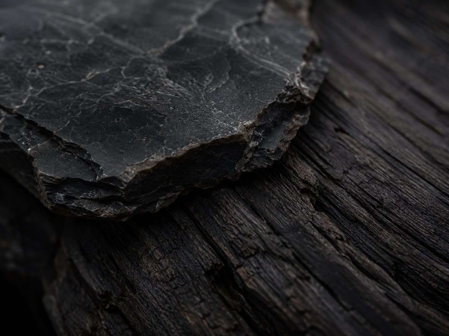 Natural black obsidian stone and raw wood surfaces used to create intentional space under soft chiaroscuro lighting