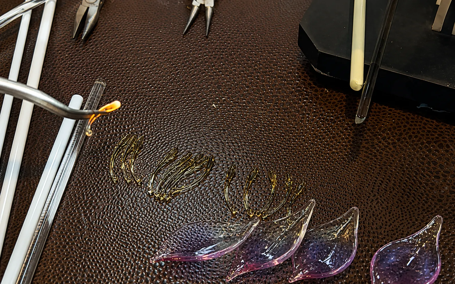 Borosilicate glass rods, handmade lotus parts, and lampworking tools arranged on a workshop table
