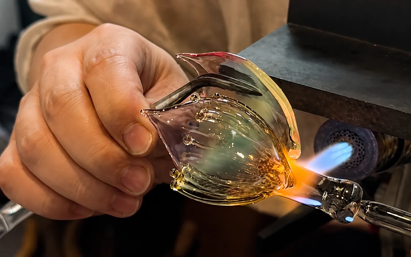 Close view of an artisan shaping a curved borosilicate glass lotus petal beside a lampworking flame